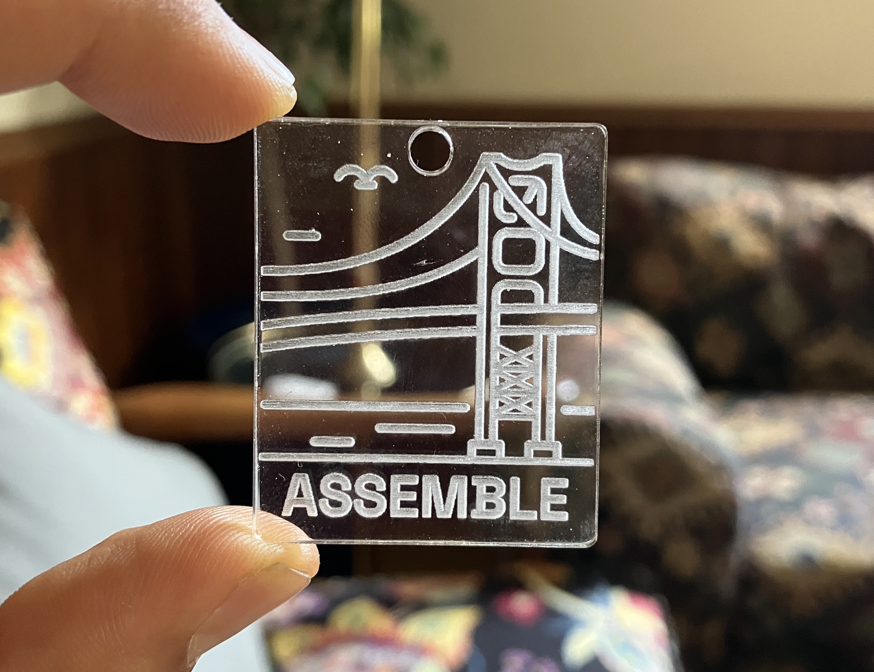Translucent rectangular piece engraved with the Assemble logo, held in between two fingers.